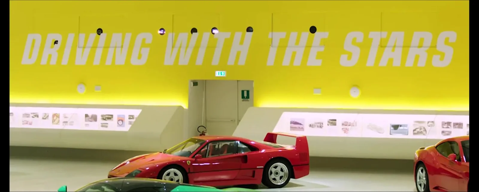 La parete gialla della mostra «Driving with the Stars», con le vetture allineate sotto il titolo