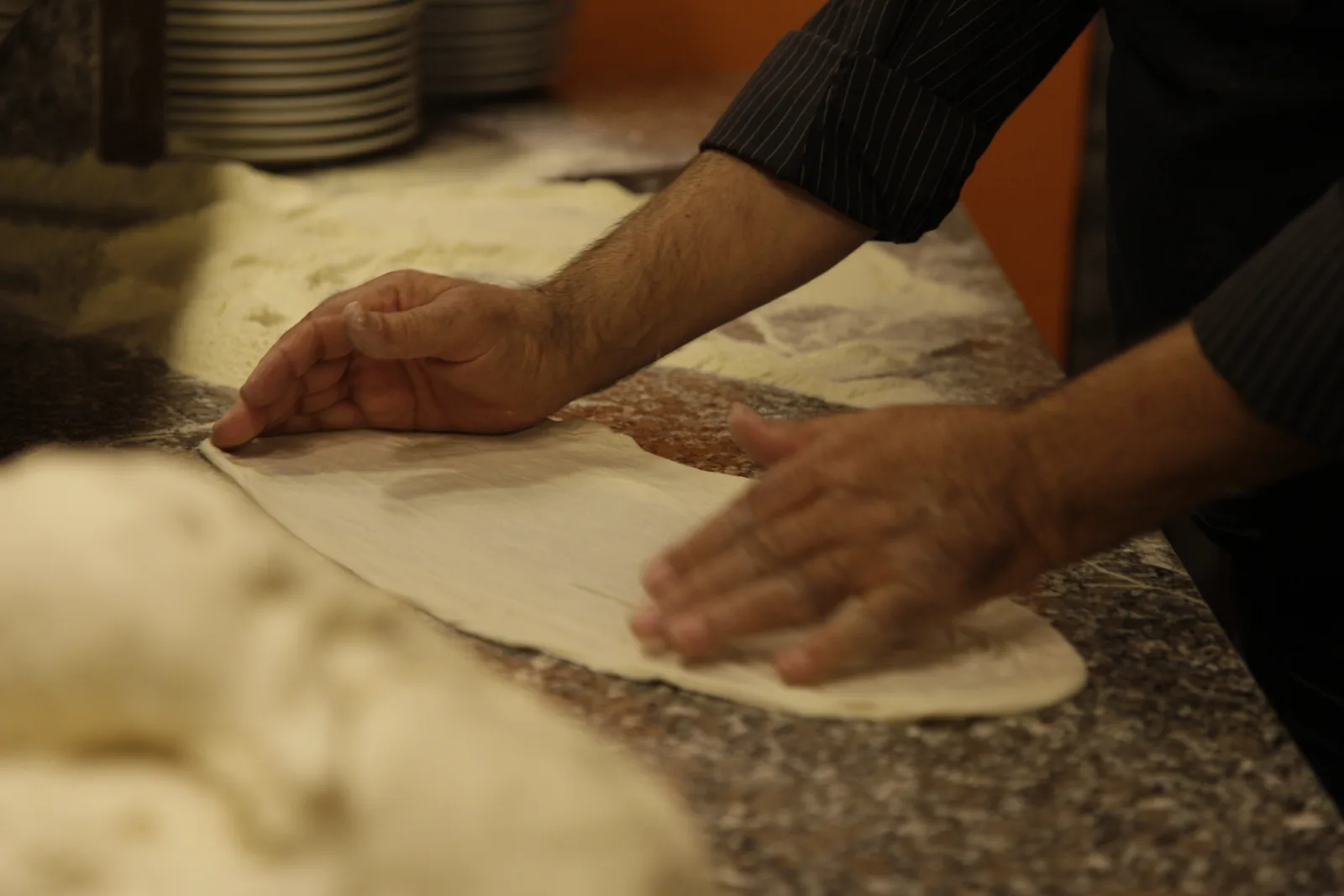 Le mani del pizzaiolo che stendono l'impasto sul banco