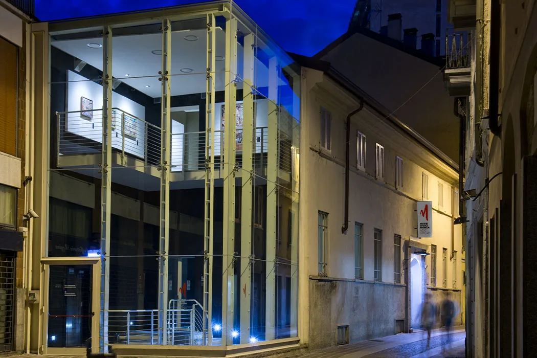 L'ingresso della Casa degli Umiliati di sera, con la scala vetrata illuminata di blu